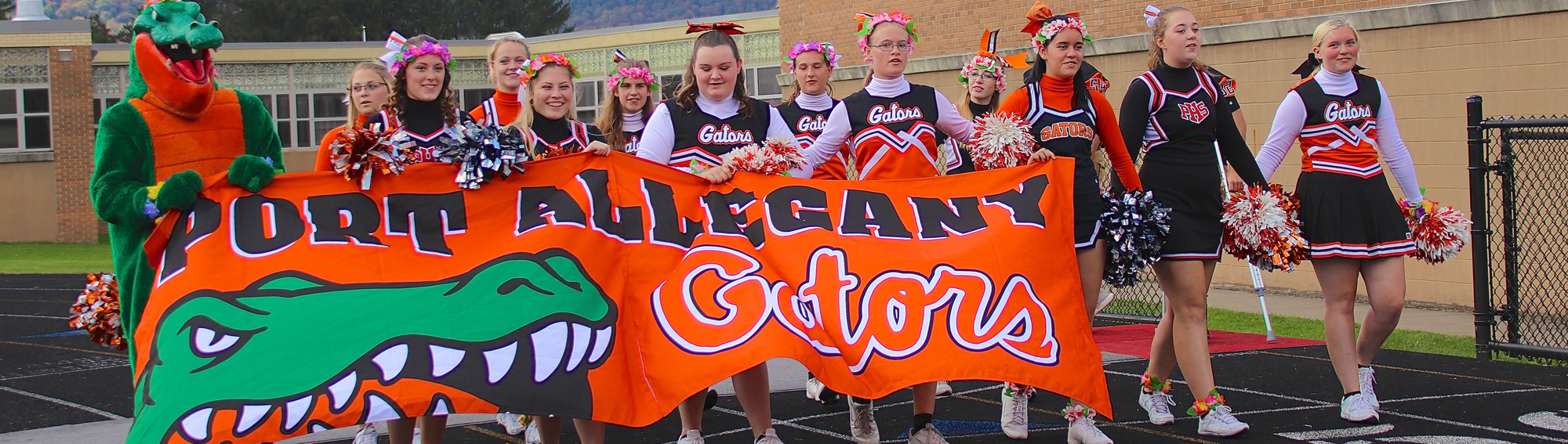 gator mascot and cheerleaders hold a banner that says Port Allegany Gators
